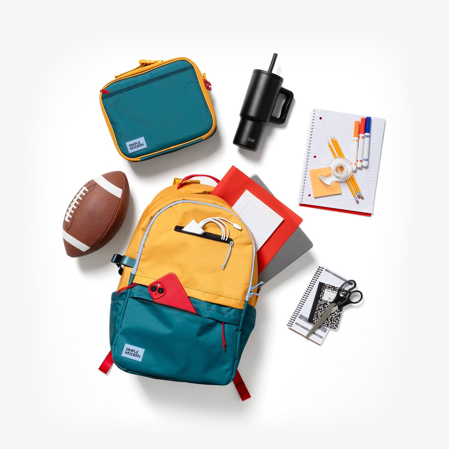 Colorful 25L Simple Modern backpack in golden yellow and teal with red accents, displayed open with matching organizer pouch, water bottle, notebooks, football, scissors, and folder in flat-lay arrangement on white