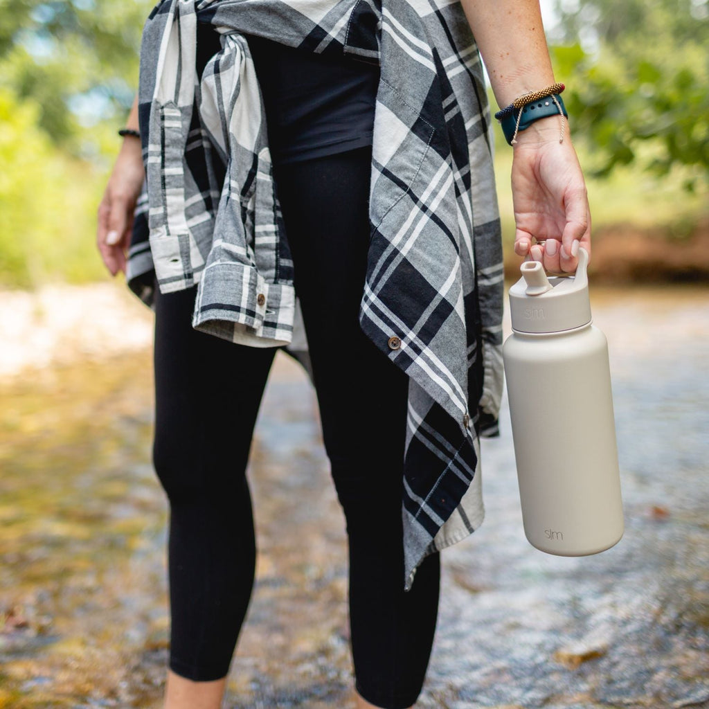 Cream-colored insulated water bottle displayed against dark black clothing background, showcasing neutral and black color palette.