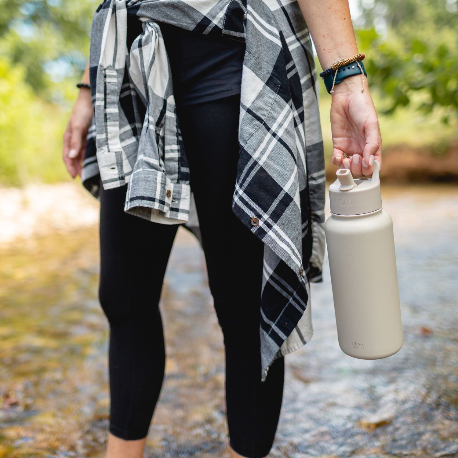 Cream-colored insulated water bottle displayed against dark black clothing background, showcasing neutral and black color palette.