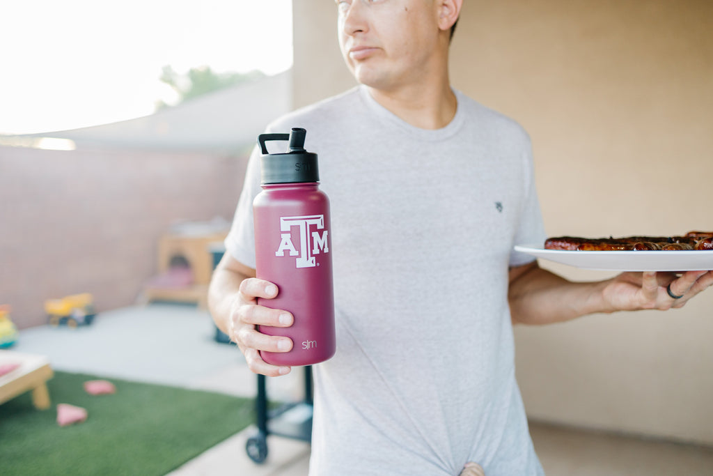 Burgundy water bottle held by person wearing light gray t-shirt against cream background