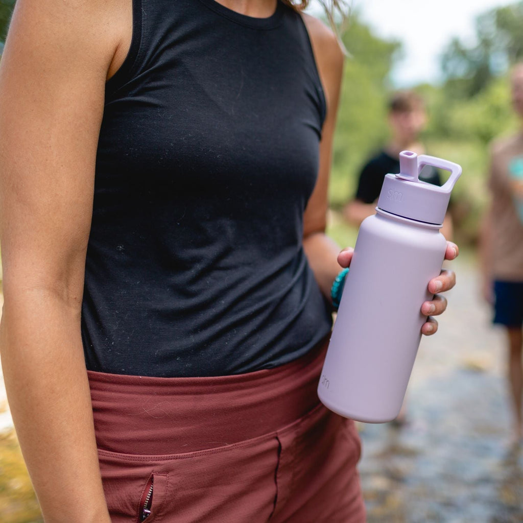 Person wearing black sleeveless tank top holding a soft lavender water bottle against their chest, with warm medium skin tone visible