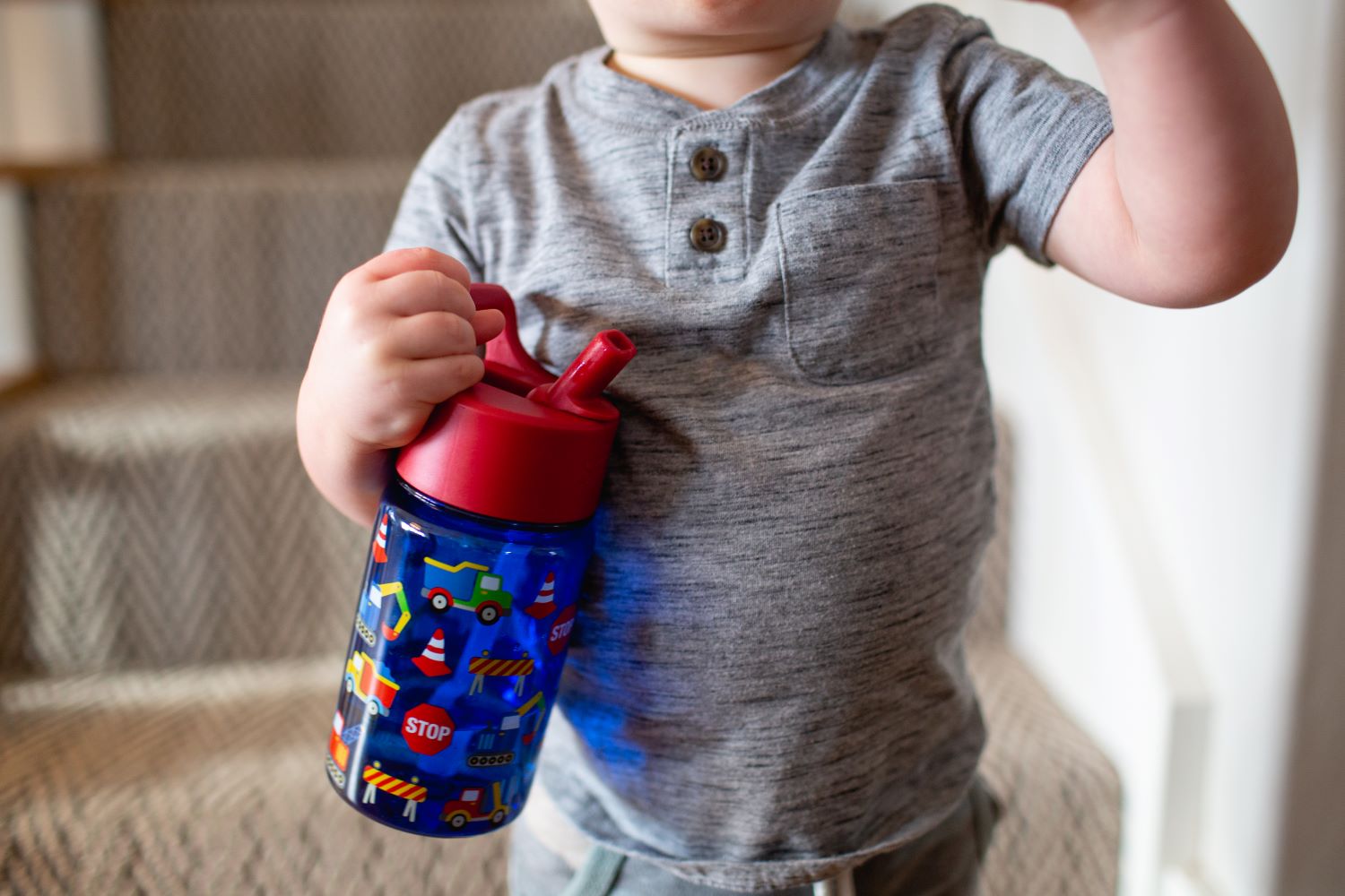 Blue water bottle with red flip-top lid held by child wearing gray heathered henley shirt