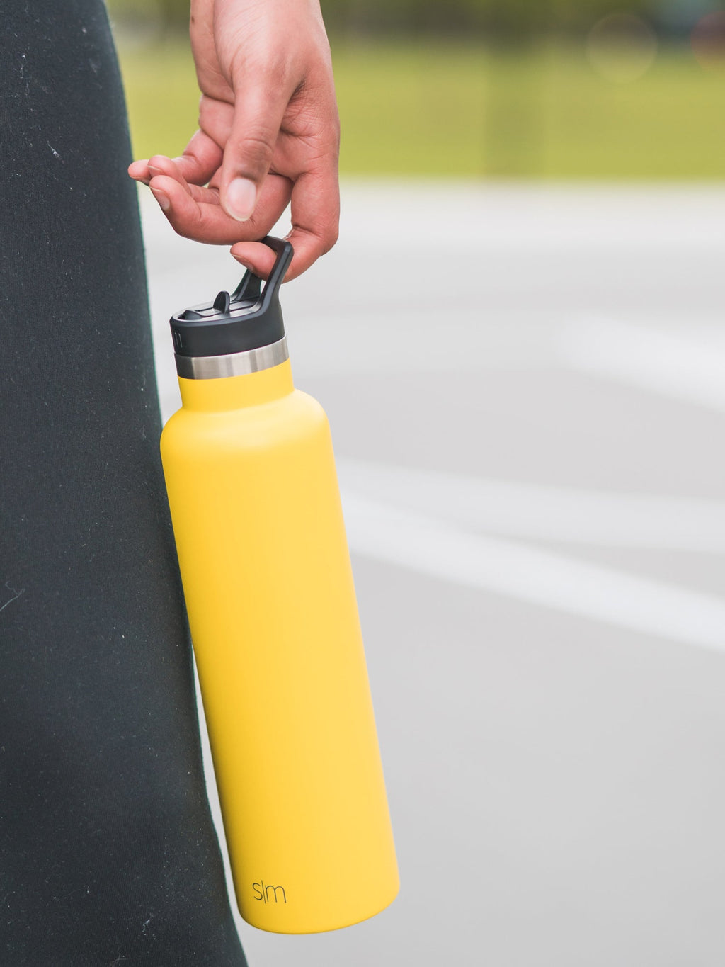 Yellow straw lid with black handle mechanism and brushed stainless steel accents, shown in use on a beverage container.
