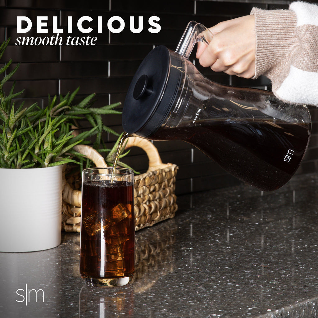 Dark cold brew coffee being poured into a glass on a black tiled countertop.