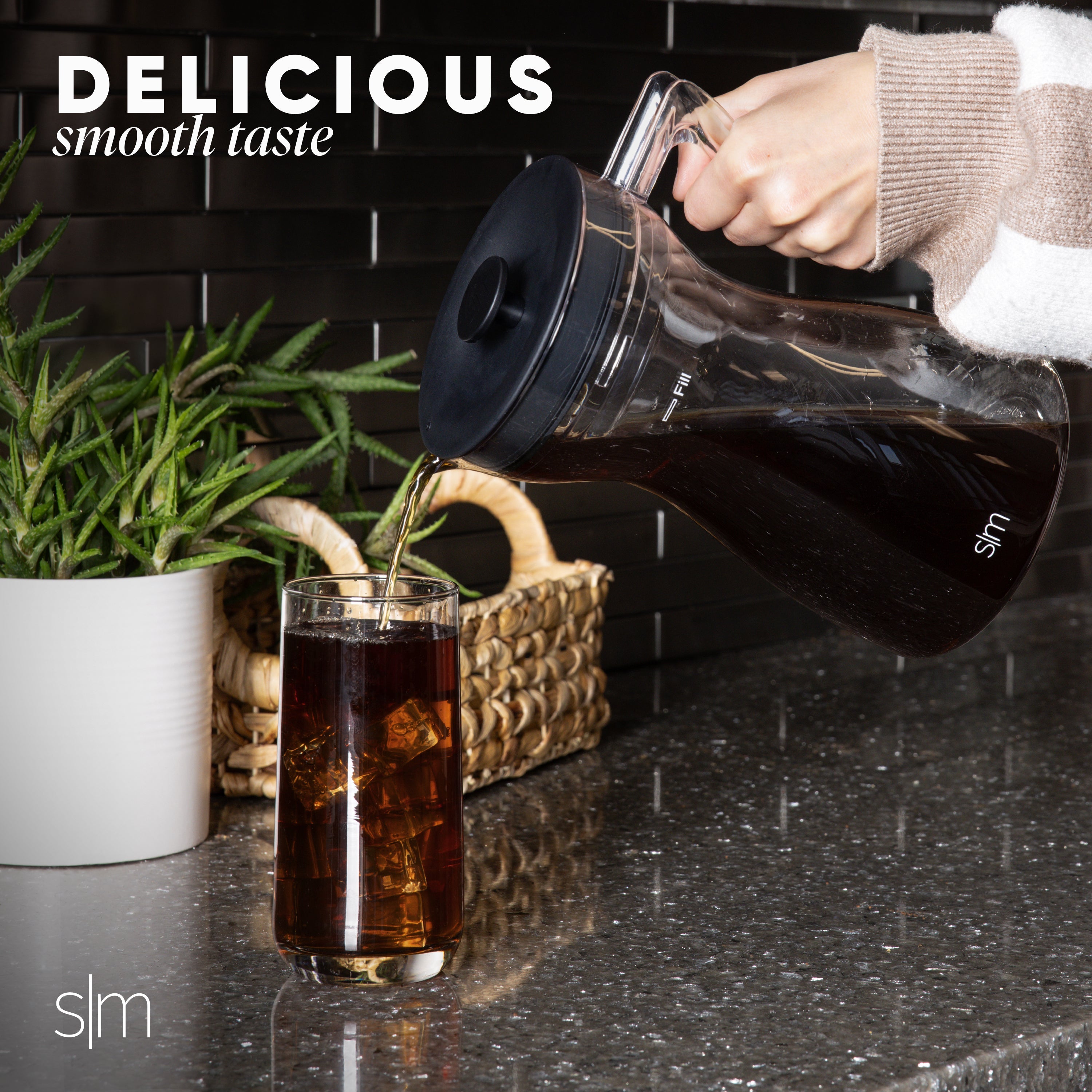 Dark cold brew coffee being poured into a glass on a black tiled countertop.