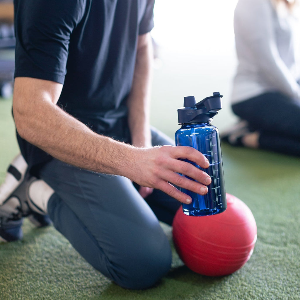 Tritan Summit 32oz water bottle in cobalt blue held by person wearing navy and charcoal athletic clothing